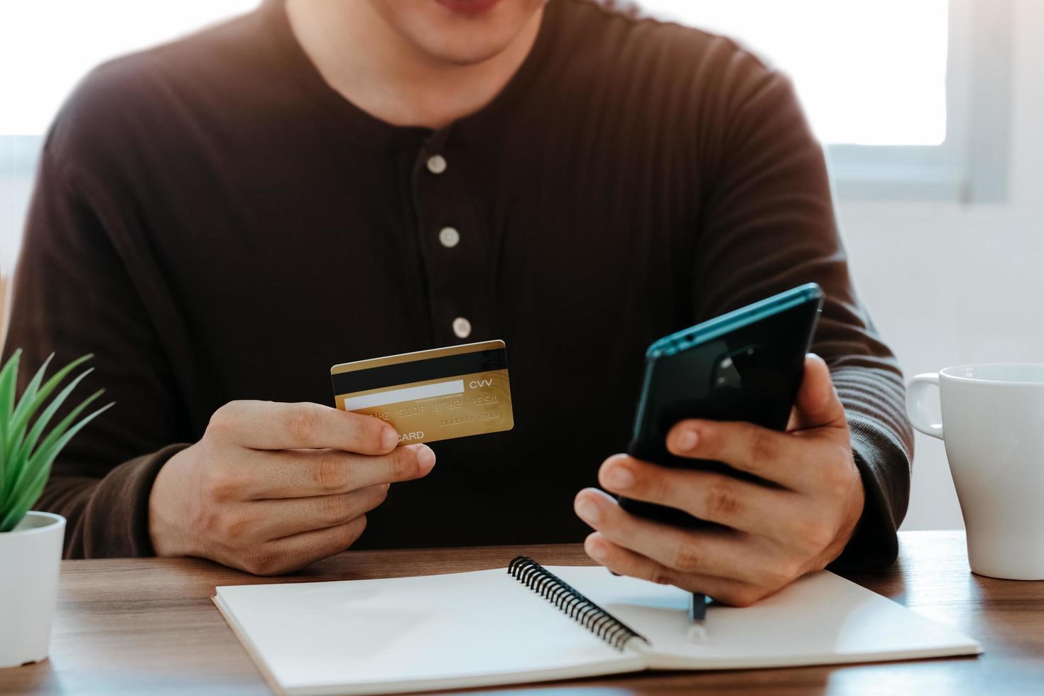 jonge man met behulp van slimme telefoon en creditcard om online te winkelen in het café van de coffeeshop. foto