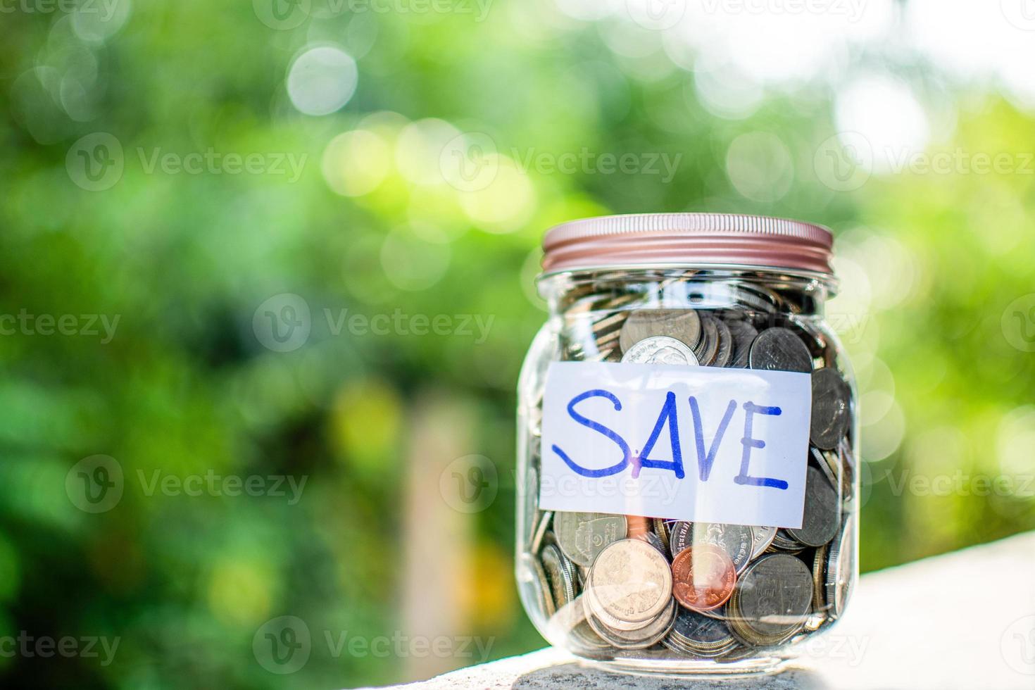 onscherpe achtergrond, munten en tekst opslaan in een glazen pot op een houten tafel. concept van geld besparen voor investeringen en noodsituaties of tijdens de uitbraak van het coronavirus covid-19. detailopname foto