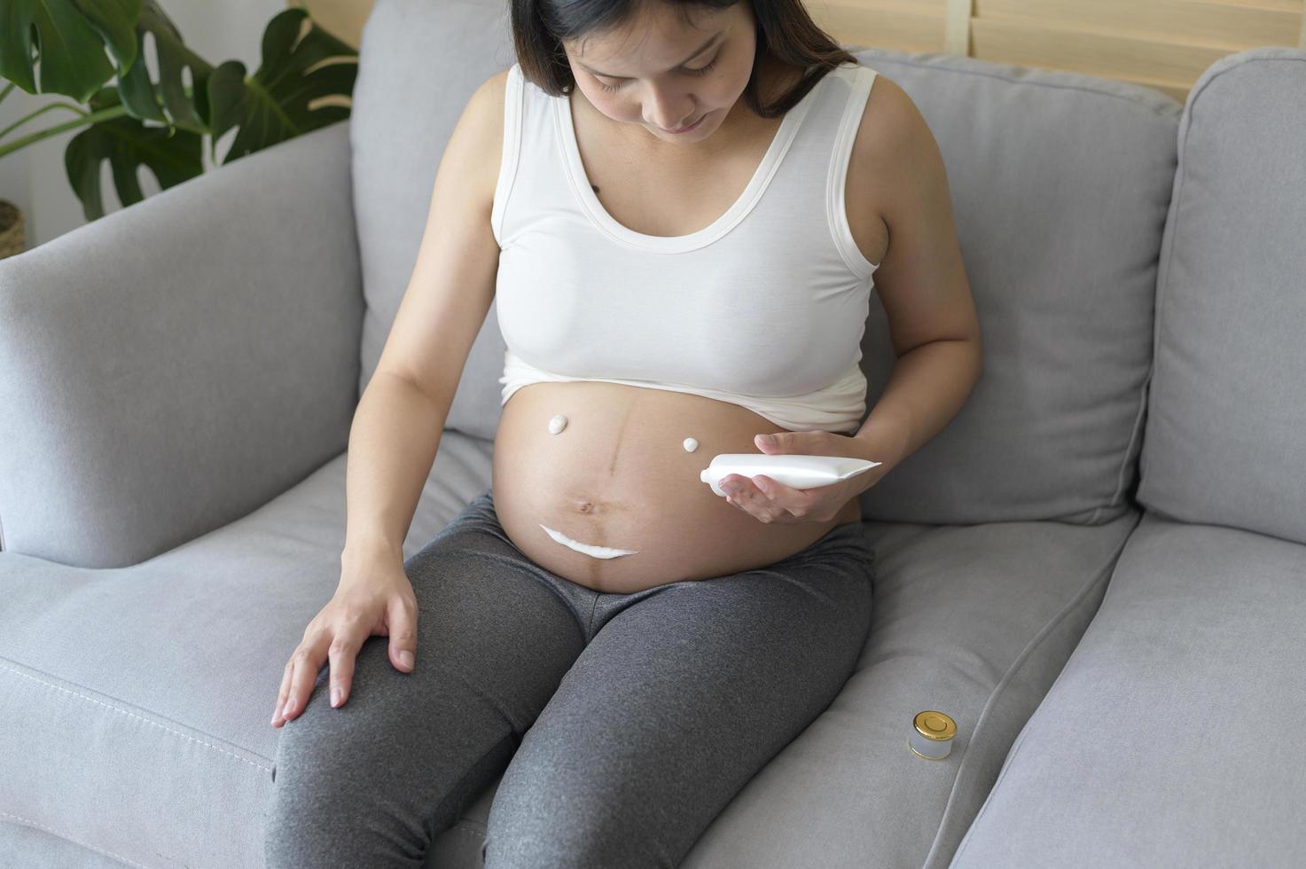 jonge zwangere vrouw die vochtinbrengende crème aanbrengt op buik, gezondheidszorg en zwangerschapszorg foto