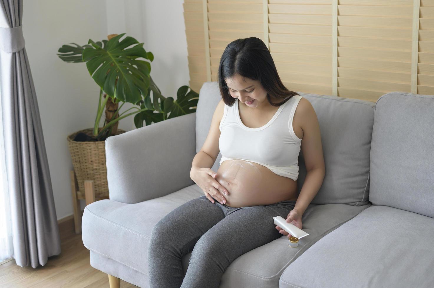 jonge zwangere vrouw die vochtinbrengende crème aanbrengt op buik, gezondheidszorg en zwangerschapszorg foto