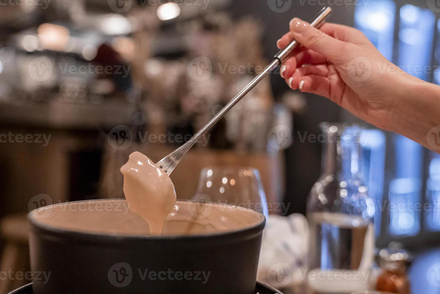 vrouwelijke toerist die voedsel dompelt in kaasfondue aan tafel in restaurant foto