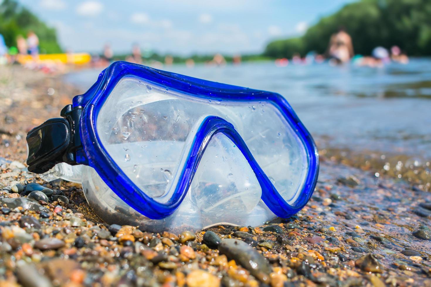 een zwemmasker ligt op een openbaar strand in de buurt van het water tegen de achtergrond van vakantiegangers foto