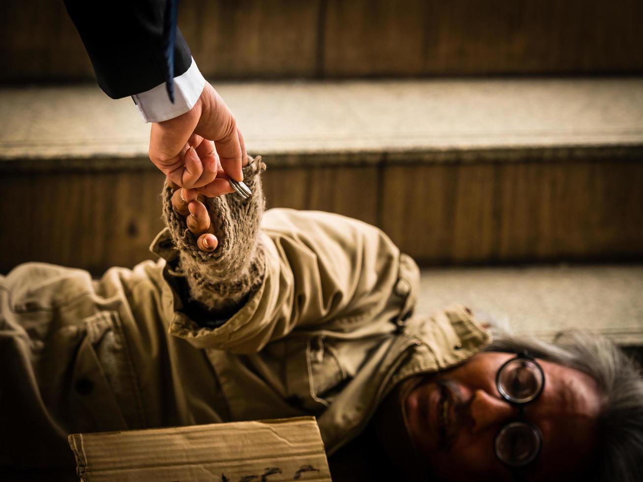 een zakenman geeft geld aan een dakloze man die op een ladder slaapt foto