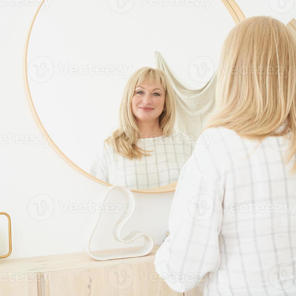 vrouw van middelbare leeftijd kijkt naar zichzelf. rijpe mooie blonde vrouw met lang haar bewondert reflectie foto