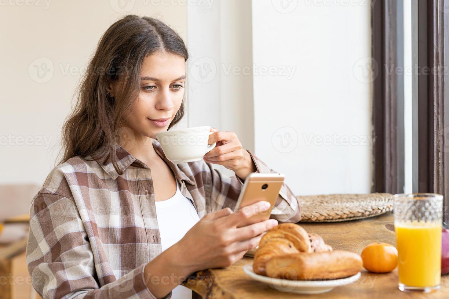 vrouw die sociale netwerken bekijkt met behulp van mobiel, genietend van een gezond ontbijt. foto