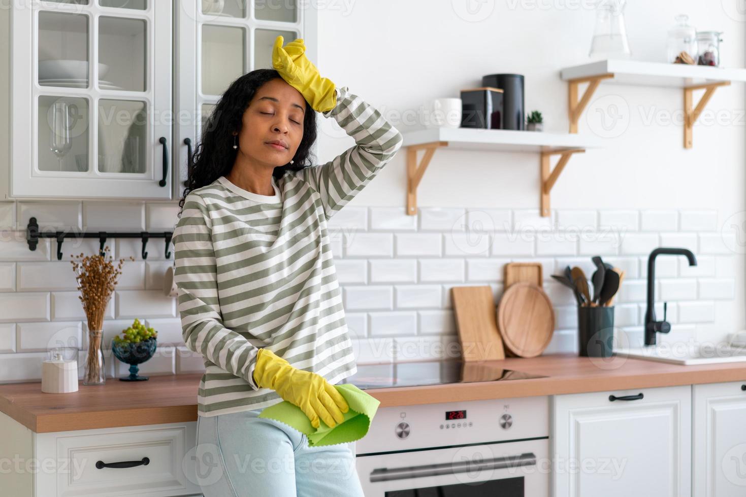 Afro-Amerikaanse vrouw klaar met het schoonmaken van de keuken. moe van stofverwerking. concept van huishoudelijk werk foto