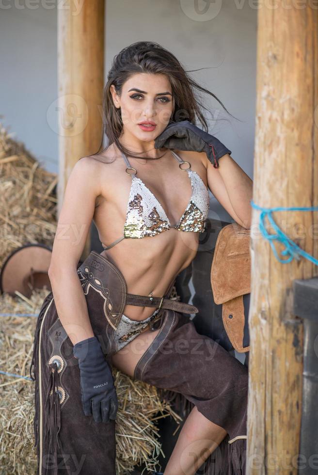 sensuele brunette vrouw met een sexy country look. portret van een meisje met voorhoofd lingerie, cowboy leren broek en handschoenen. meisje interactie en plezier op de ranch. Amerikaanse sexy landelijke stijl foto