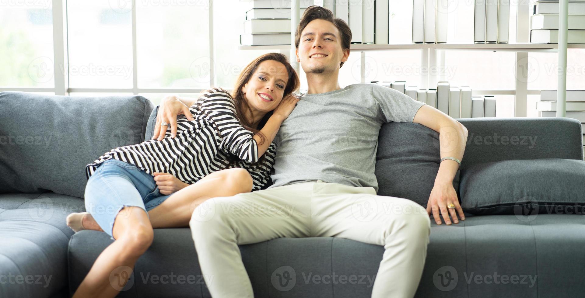 romantisch aanhankelijk paar omarmen, zittend op een gezellige bank in de woonkamer ontspannen thuis, een hechte relatie. jong familieportret glimlachend dolblij man en vrouw gelukkig vrije tijd samen. foto