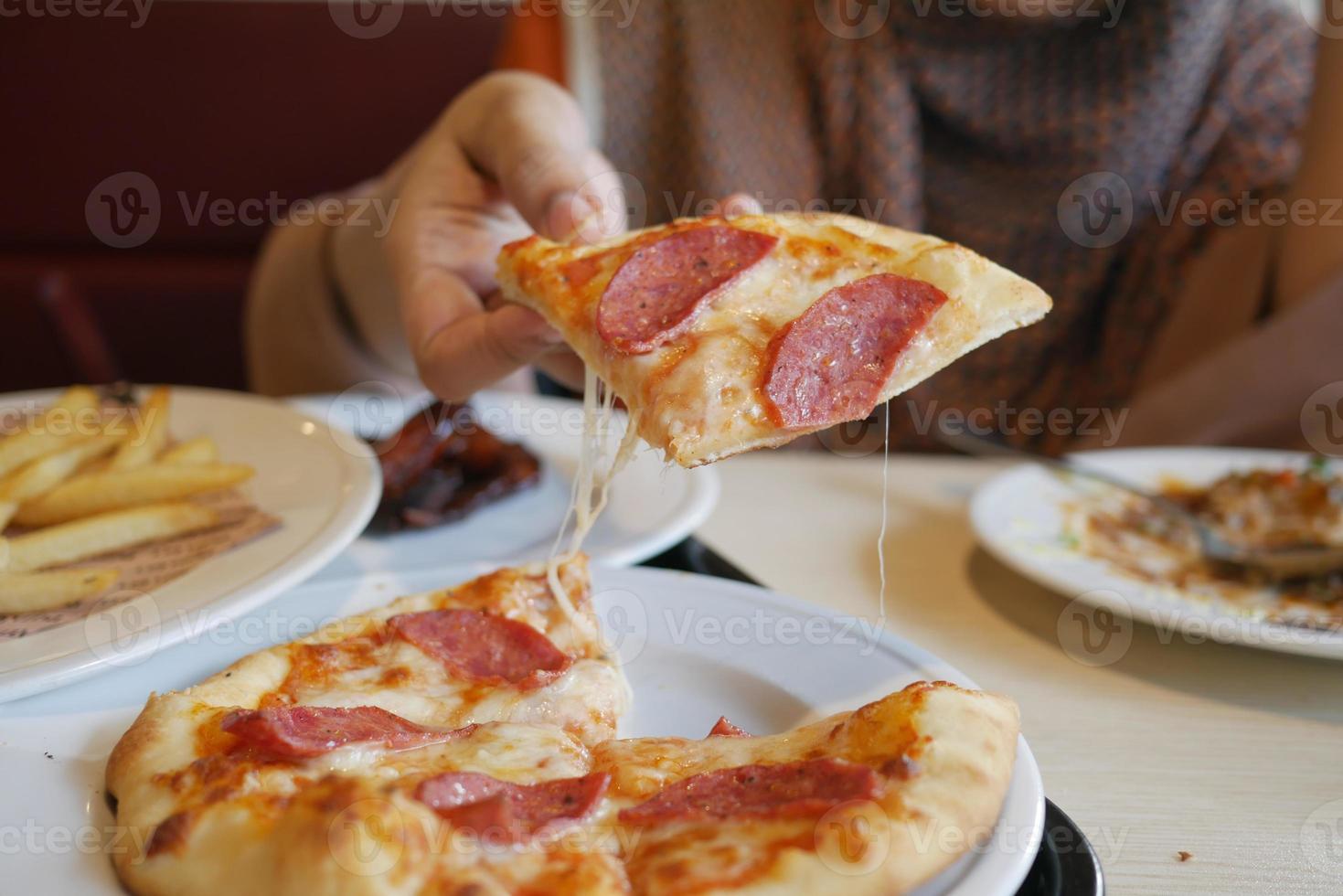 vrouwen die met de hand een stuk pizza van een bord plukken foto