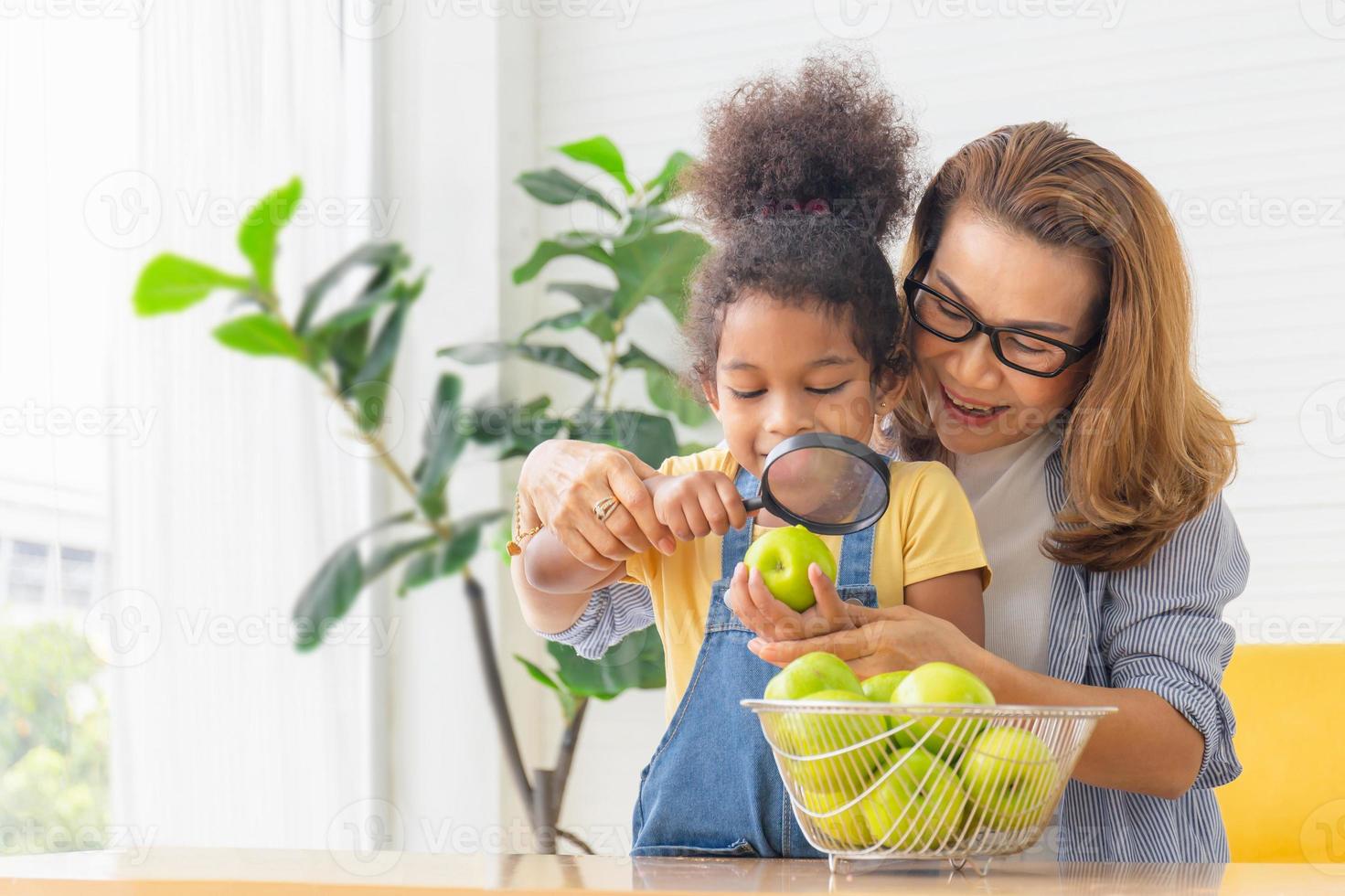 moeder en dochter kijken naar appel met vergrootglas, grootmoeder en kleinkinderen spelen vrolijk in de woonkamer foto