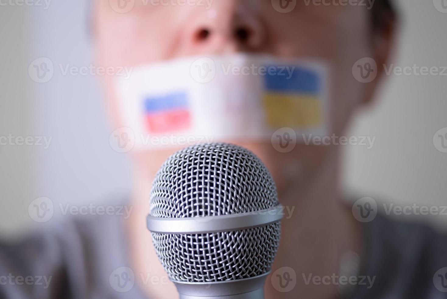 een mond met ducttape en een vlag van rusland en oekraïne die in een microfoon probeert te spreken. foto