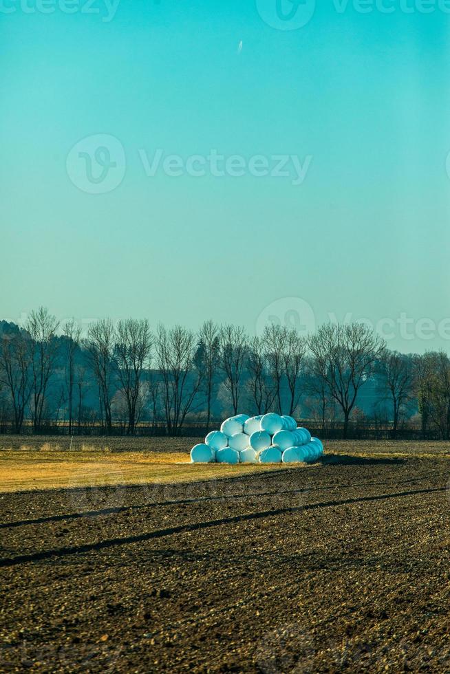 stapel in plastic verpakte hooibalen door geploegd veld foto