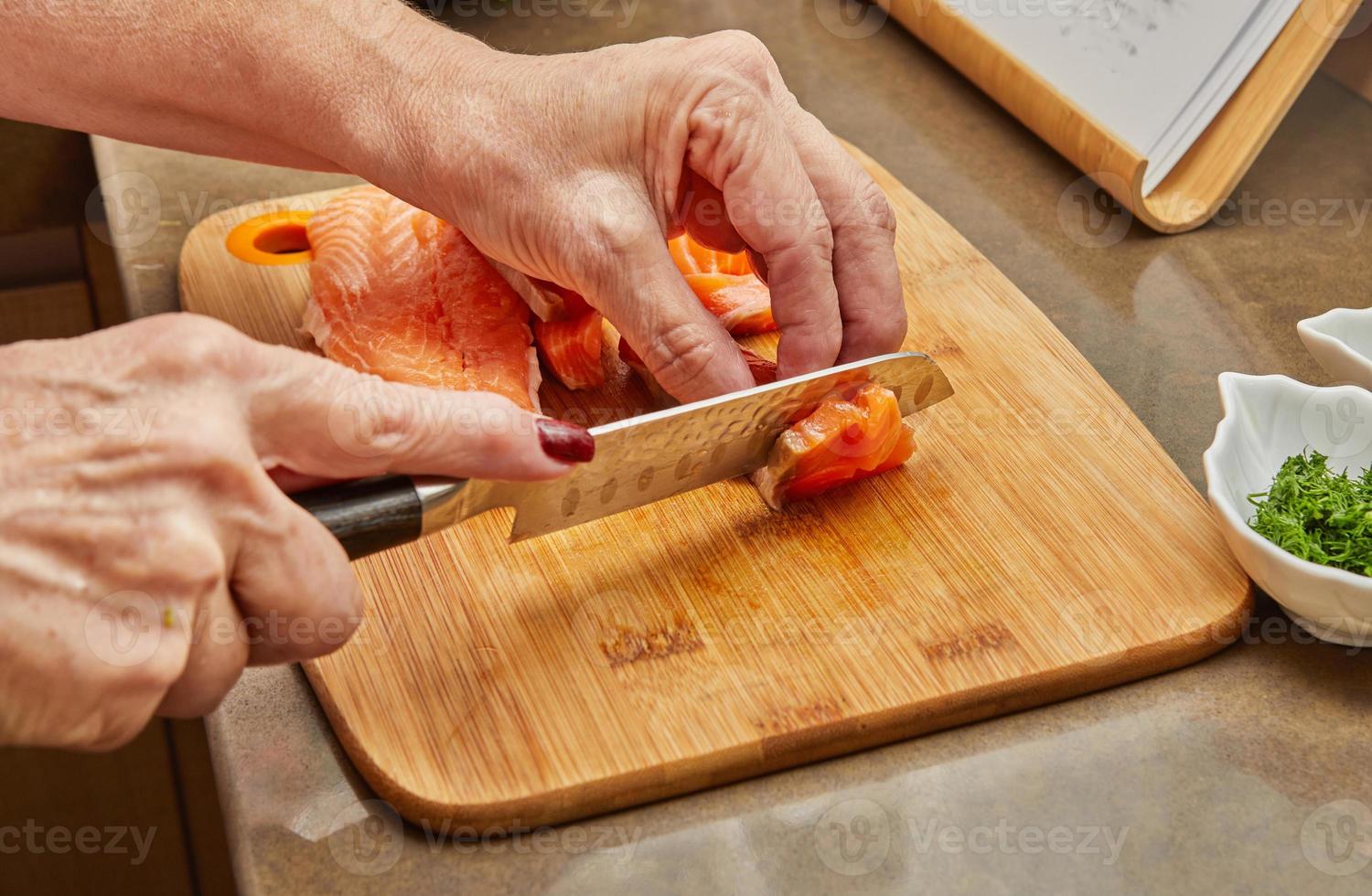 chef-kok snijdt de zalm in blokjes met mes om het gerecht te bereiden volgens het recept foto