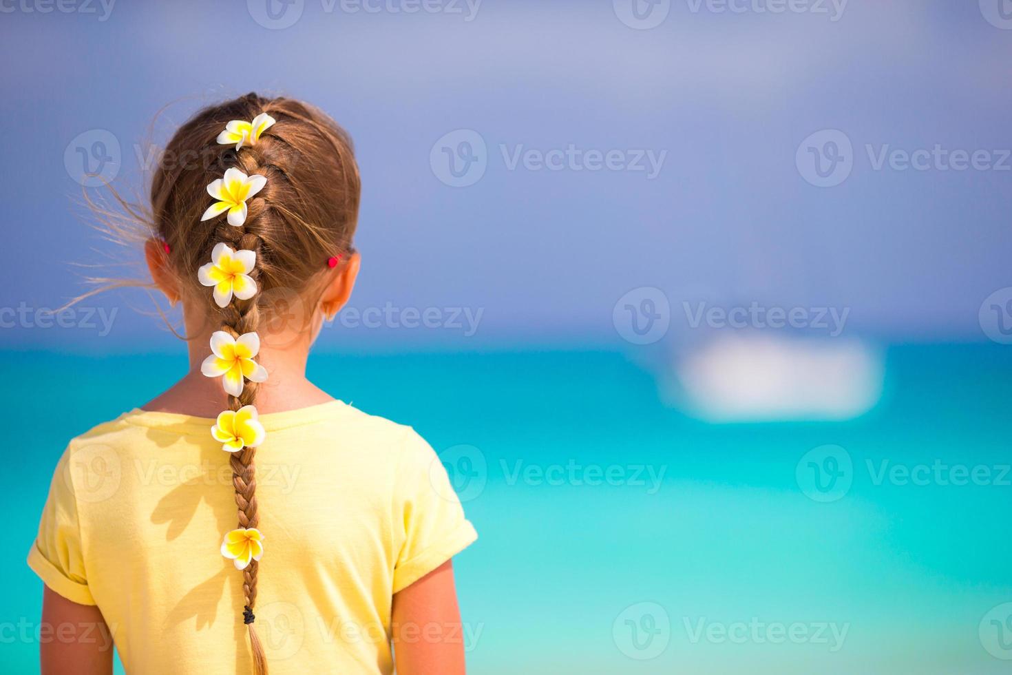 schattig klein meisje met frangipani bloemen in haar op het strand foto