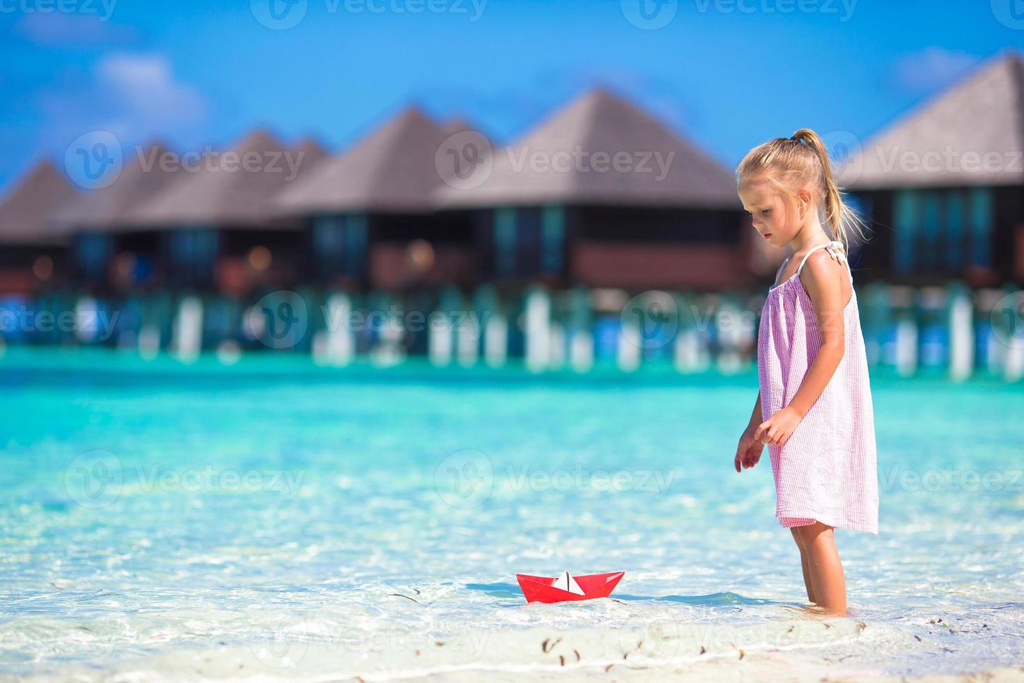 schattig klein meisje speelt met papieren boot in turquoise zee foto