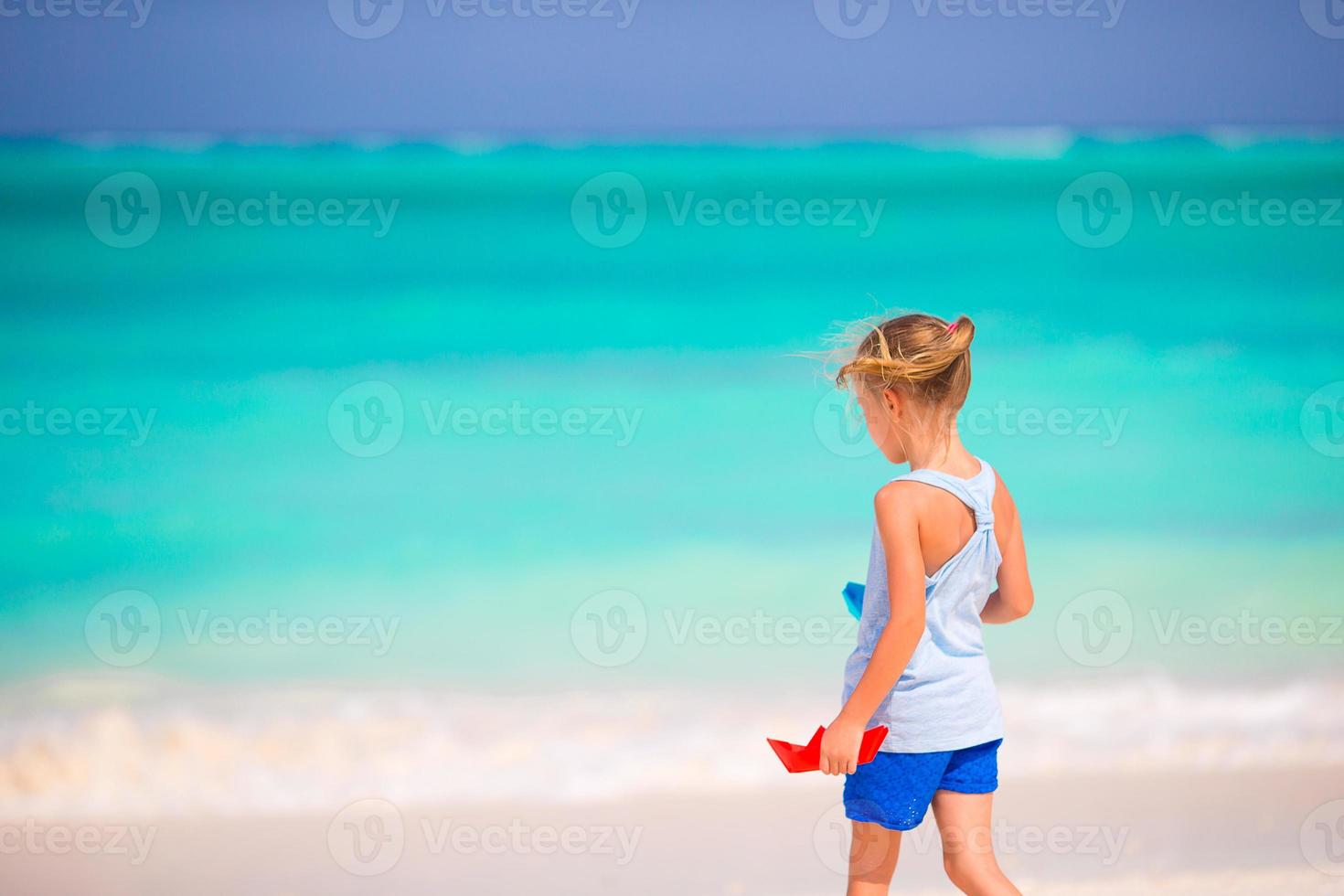 schattig klein meisje speelt met origami boot in turquoise zee foto