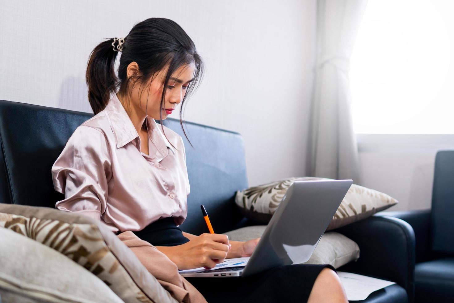 portret van een jonge vrouw die op de bank zit met een laptop, een vrouw die een laptop gebruikt en aantekeningen maakt op een gezellige bank foto