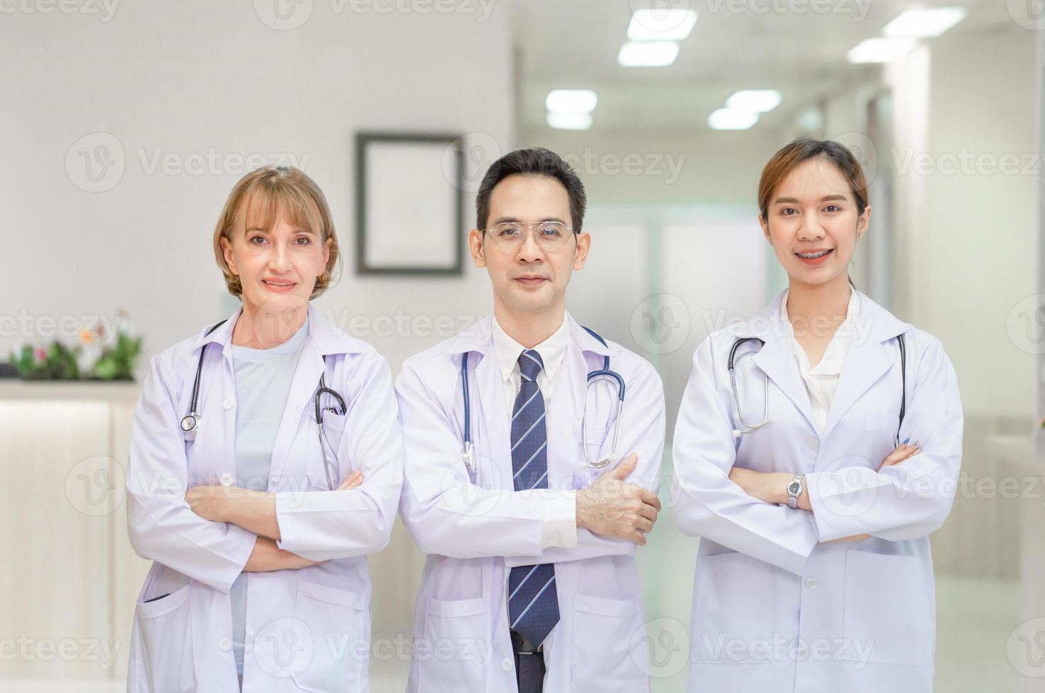 team van artsen kijken naar de camera en glimlachen terwijl ze met gekruiste armen in het ziekenhuis staan, artsen staan als een team met gekruiste armen foto