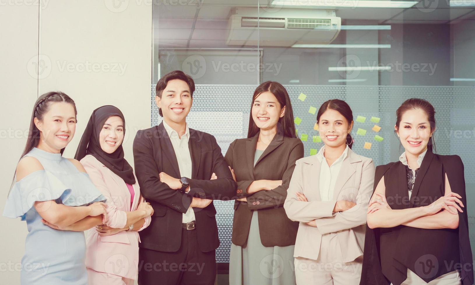 groep jonge mensen glimlachen en armen gekruist op kantoor werkplek, succesvol business team staan en kijken naar camera met gekruiste armen op kantoor foto