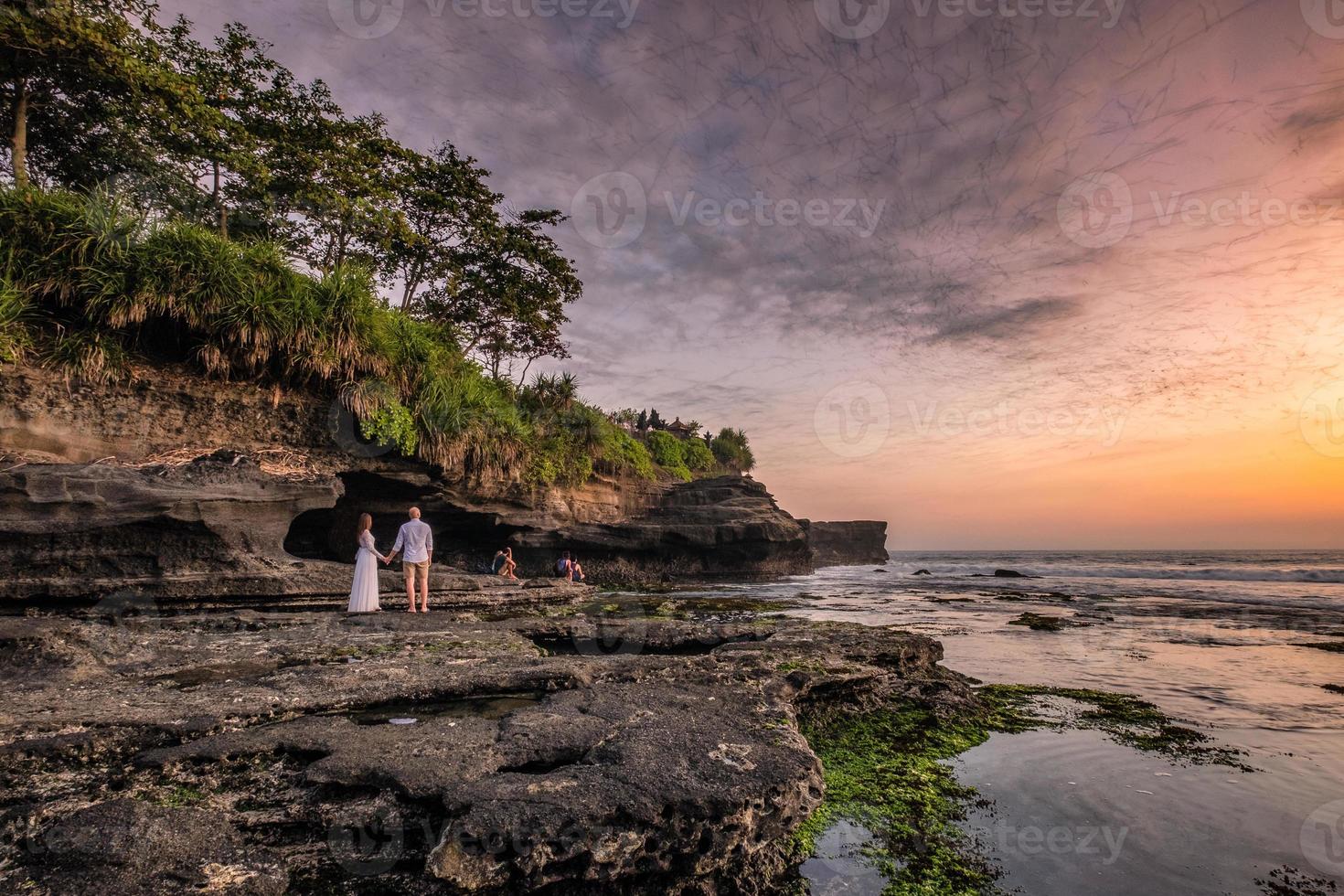 liefhebbers kijken bij zonsondergang naar een zwerm vleermuizen vanuit een grot aan de kust foto