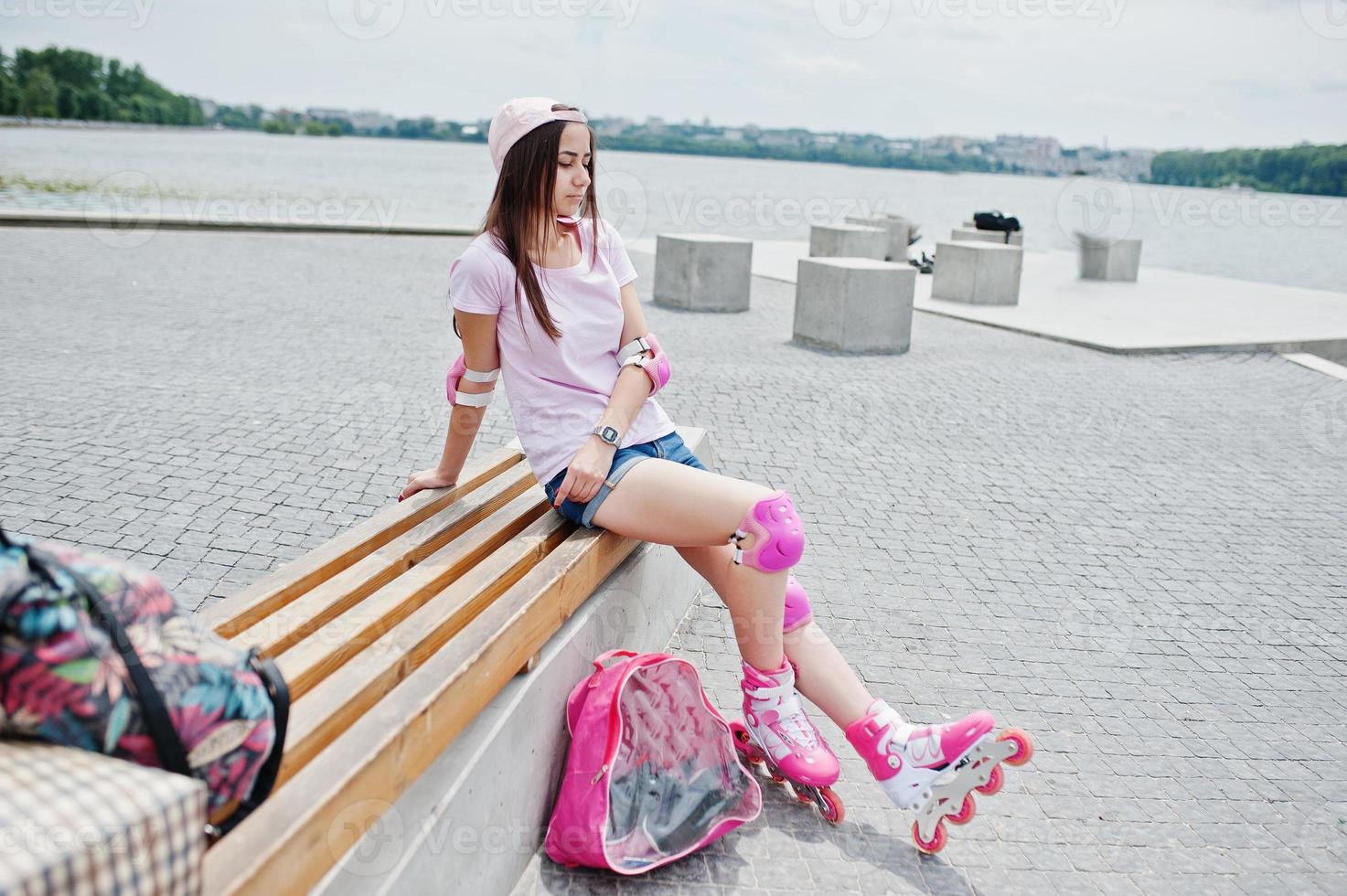 fantastische jonge vrouw in casual kleding en pet zittend op de bank in het skatepark met skeelers aan. foto