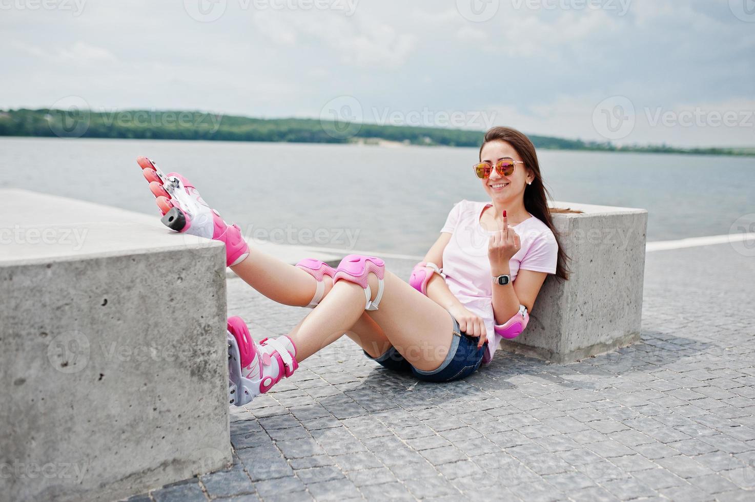 portret van een mooie vrouw zittend op de grond naast betonnen kubus en wijzende middelvinger. het dragen van skeelers en vrijetijdskleding. foto