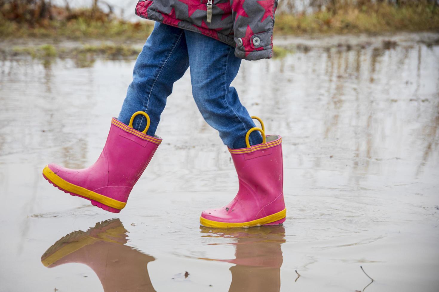 klein meisje met roze laarzen lopen op een modderig pad foto