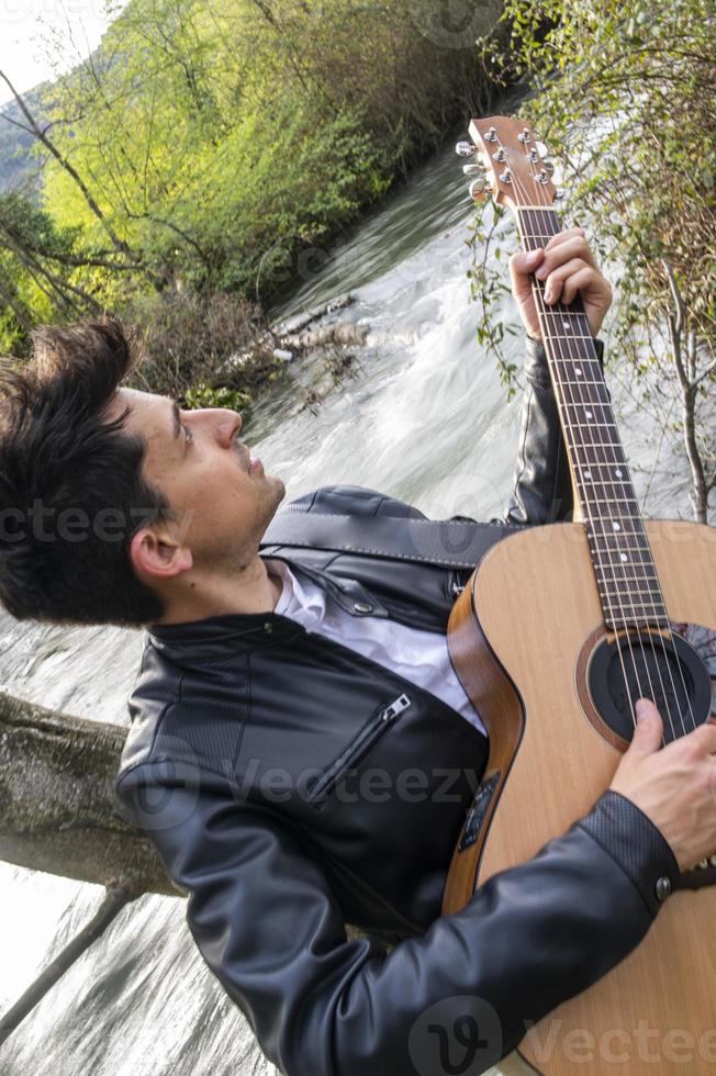 jongen speelt gitaar bij de rivier foto