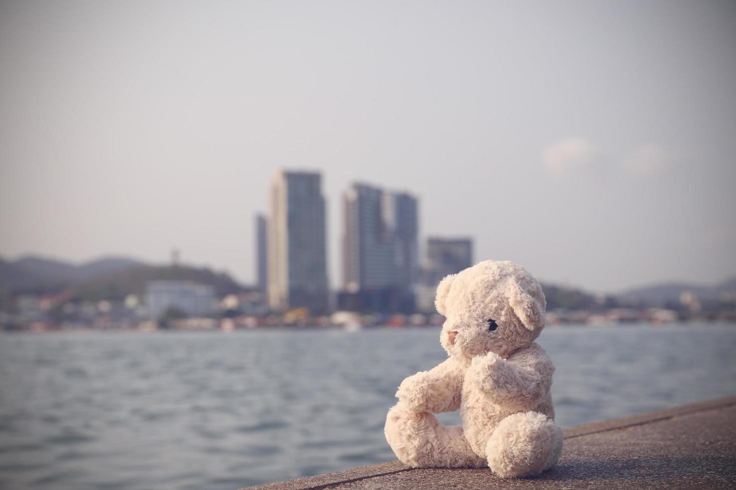 een bruine pluizige teddybeer zit op een enkele brug met uitzicht op de zee met een achtergrond van een kopieerruimte. eenzaam, eenzaamheid is zinloos. foto