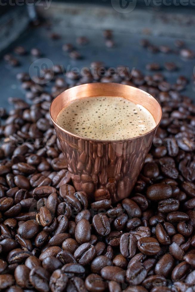 koperen kop gevuld met espressokoffie in het midden van rauwe koffiebonen verspreid op rustieke tafel foto