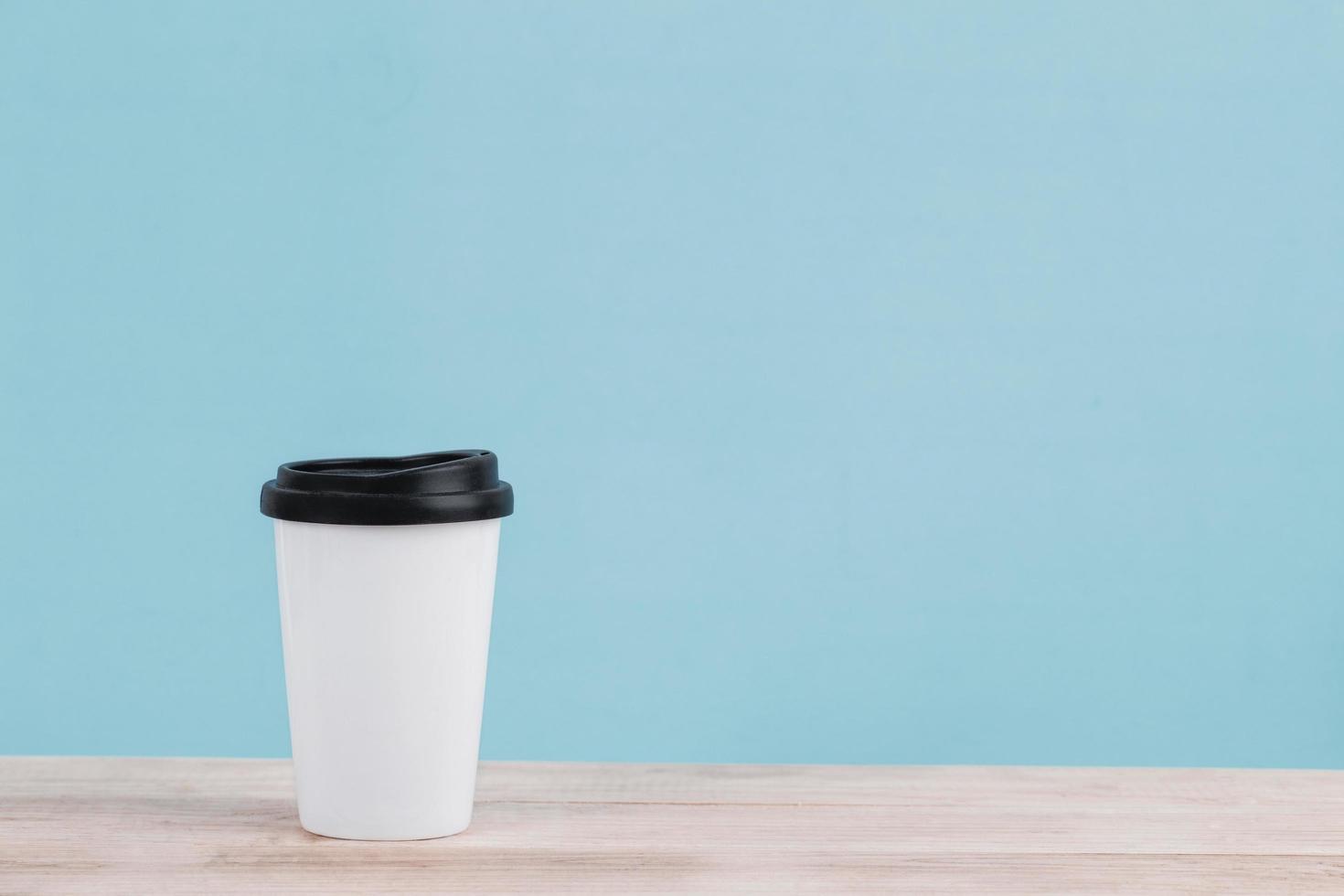 Witte koffiekopje geïsoleerd op houten tafel met blauwe achtergrond foto