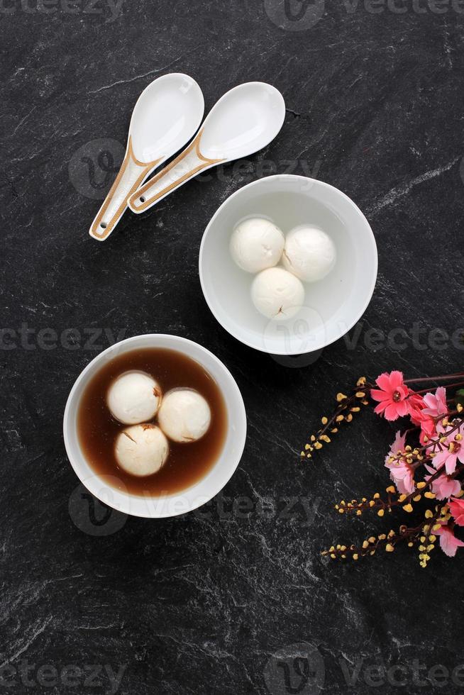 Tang yuan, chinese kleefrijst knoedel ballen met suiker gember of palmsuiker siroop op rode chinese op zwarte achtergrond voor winterzonnewende nieuwjaar festival voedsel. foto