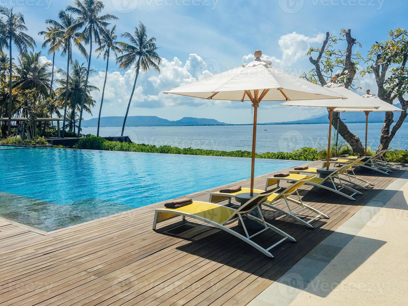 prachtig tropisch zwembad in hotel of resort met parasol, kokosnotenboom ligstoelen, palmbomen met uitzicht op het overloopzwembad, oceaan en bergachtergrond. foto