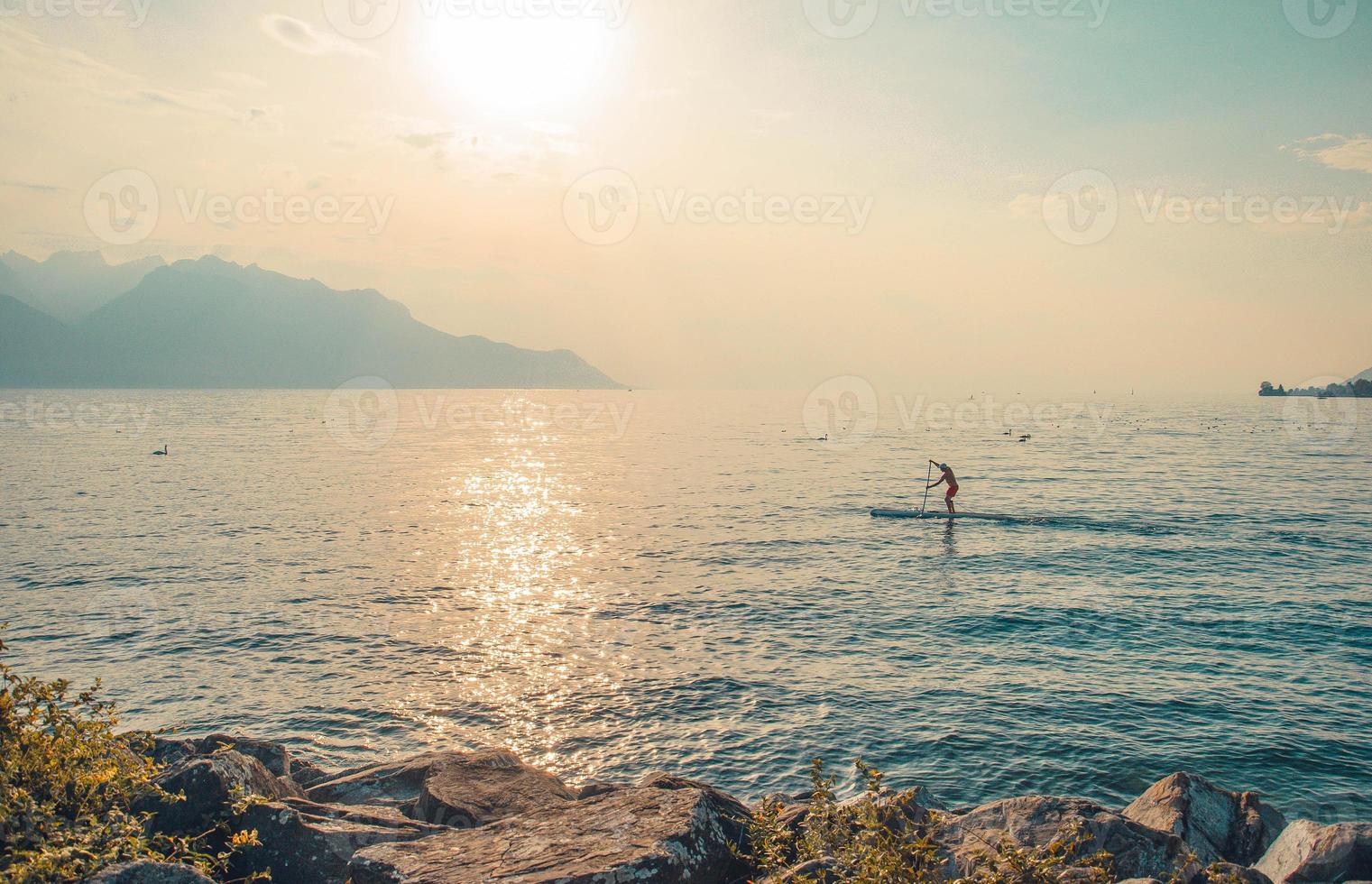 man op een surfplank met peddel op het meer van leman, zwitserland foto