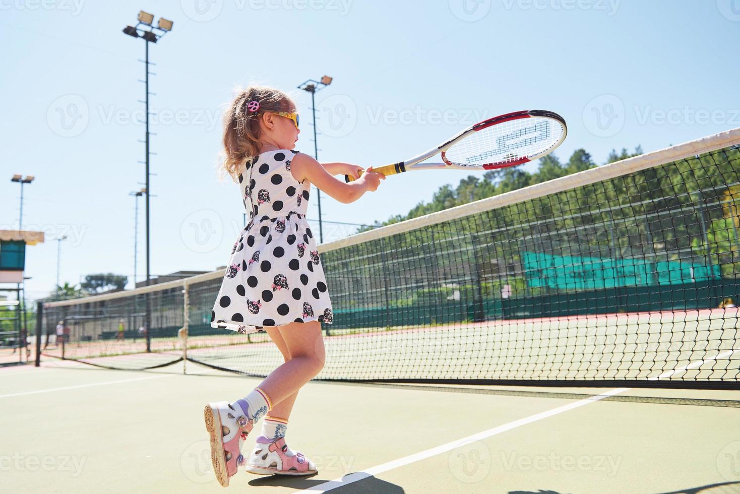 schattig klein meisje tennist buiten op de tennisbaan foto