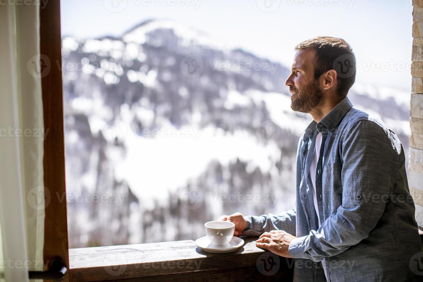 jonge man met kop hete thee bij winterraam foto