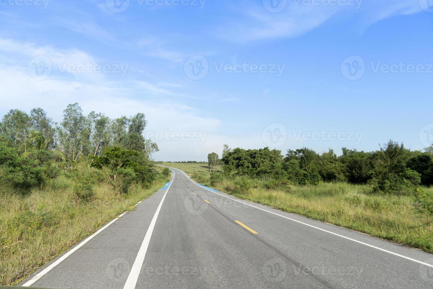 rechte weg naar voren van asfaltweg en blauwe fietspad schouderweg in thailand. naast de grond van groen gras en bomen. onder de blauwe lucht. foto