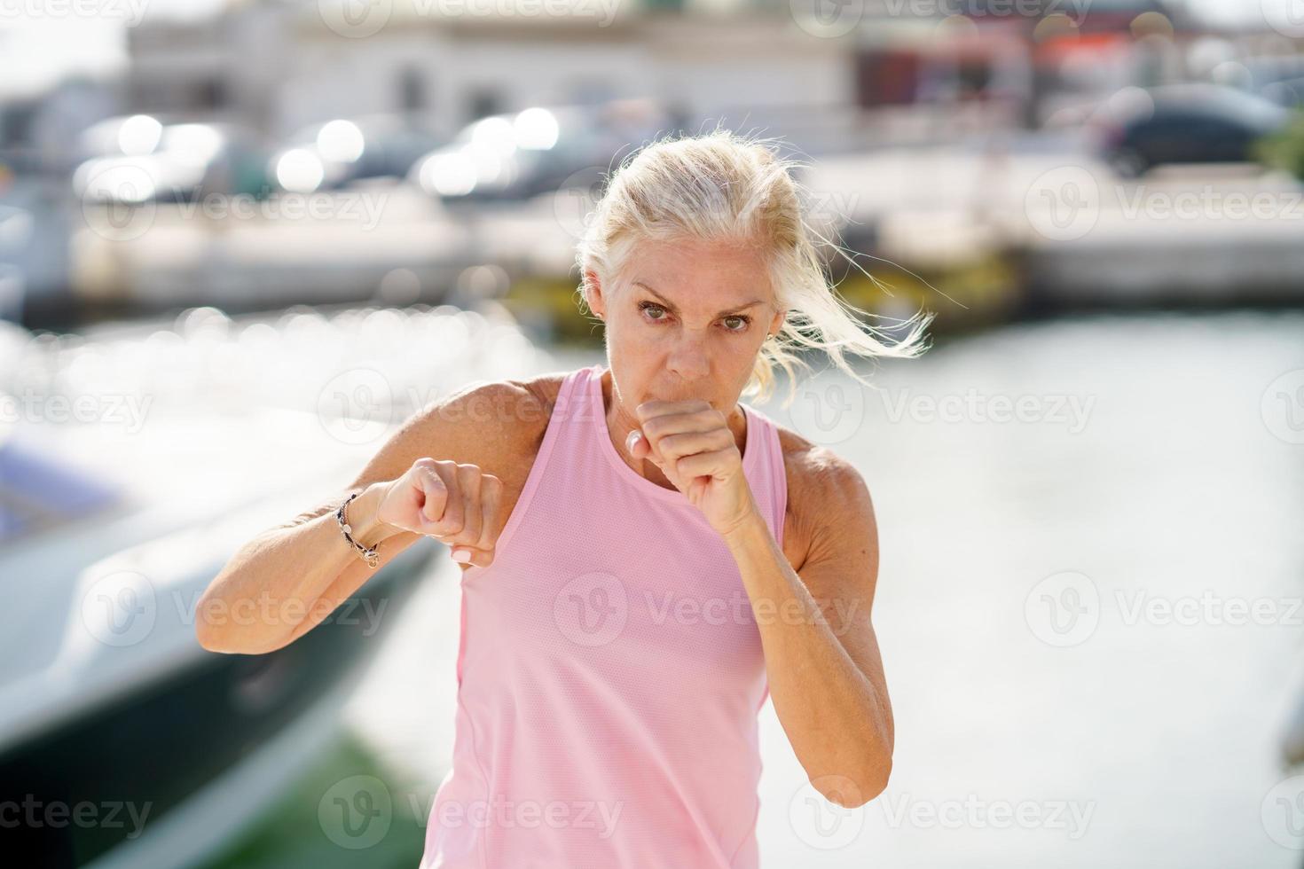 oudere vrouw die schaduwboksen buitenshuis doet. senior vrouw die sport doet in een kusthaven foto