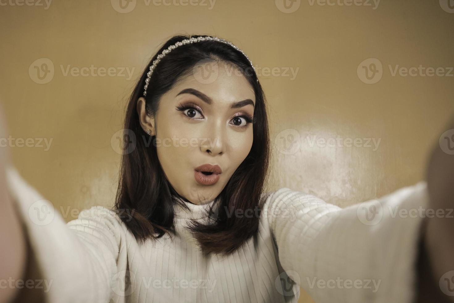 jonge aziatische vrouw is verrast en maakt selfies met haar mobiele telefoon. Indonesische vrouw op oranje achtergrond. foto