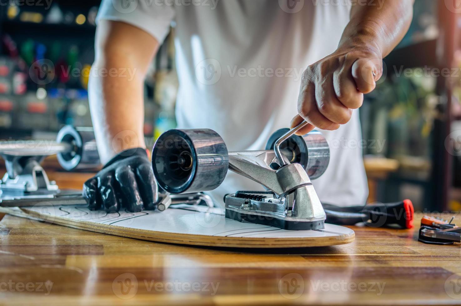 man gebruikt de socket-tool of inbussleutels om de moeren op skateboard te verwijderen en past de ophanging aan in werkplaats, skateboardonderhoud en reparatieconcept. selectieve focus op ophangset foto