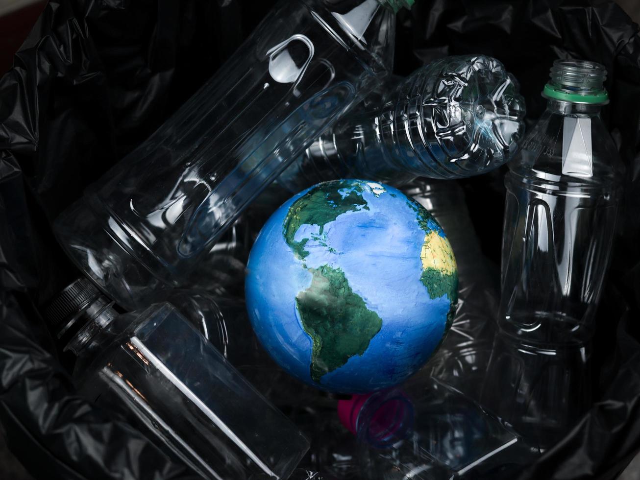 Earth Globe wordt in de vuilnisbak gegooid met plastic afval, Earth Day, ecologie en milieuconcept foto