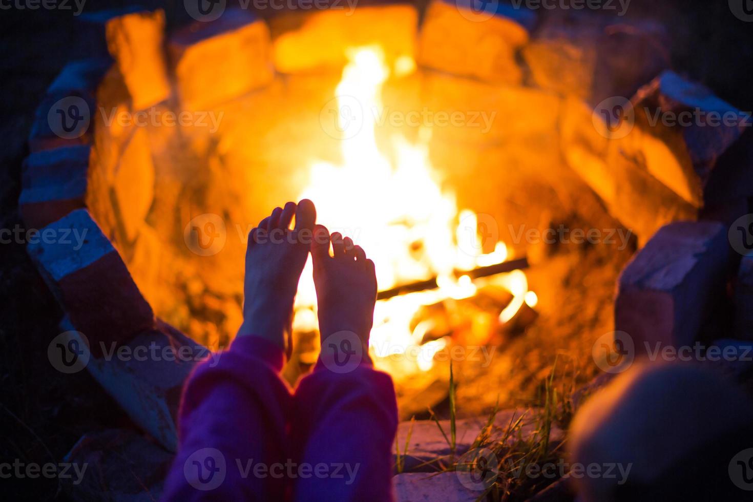 blote voeten van kind door vuur. bijeenkomsten 's nachts bij het kampvuur in de open lucht in de zomer in de natuur. familie camping trip, bijeenkomsten rond het kampvuur. camping lantaarn en tent. verwarm je voeten, koude nacht foto