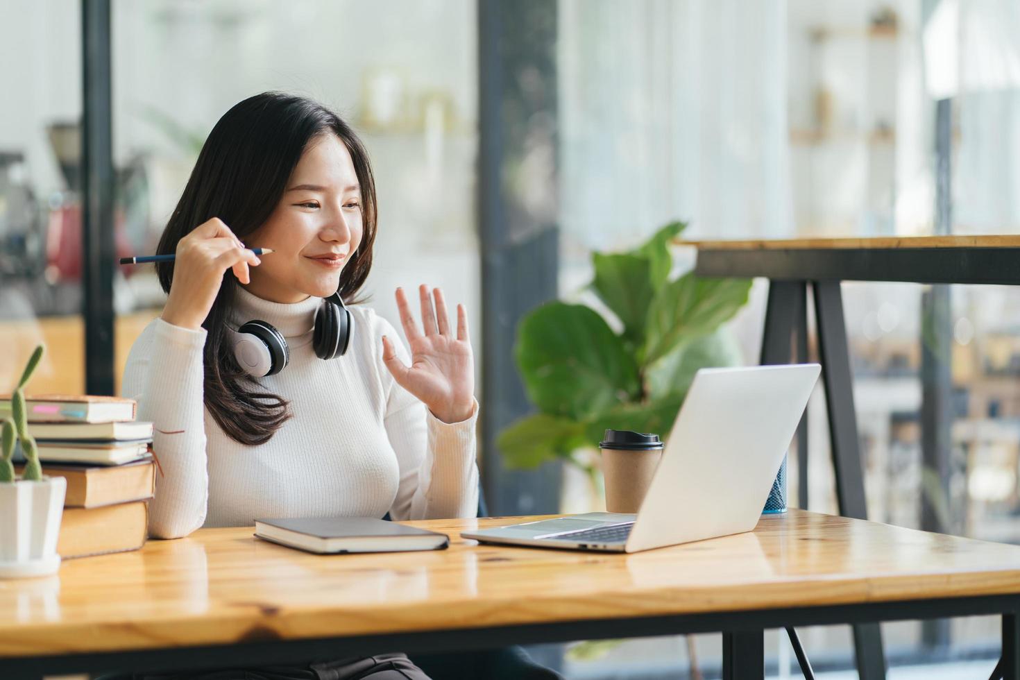 gelukkige jonge aziatische vrouw zwaaiend met de hand in gesprek met externe webleraar op sociale afstand videoconferentiegesprek e-learning klasse op computer. meisje leert thuis foto