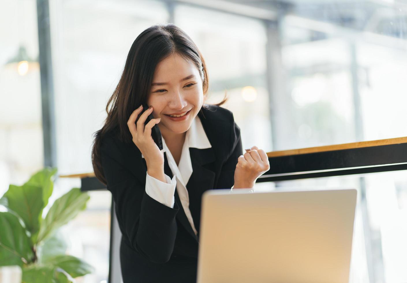 gelukkige jonge aziatische vrouw die op de mobiele telefoon praat en glimlacht terwijl ze op haar werkplek op kantoor zit. foto