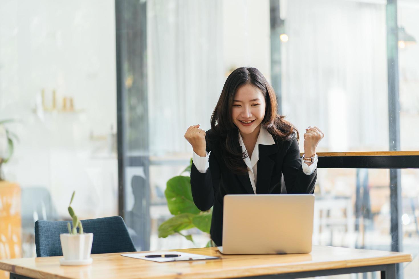 opgewonden jonge vrouw die aan tafel staat met laptop en succes viert foto