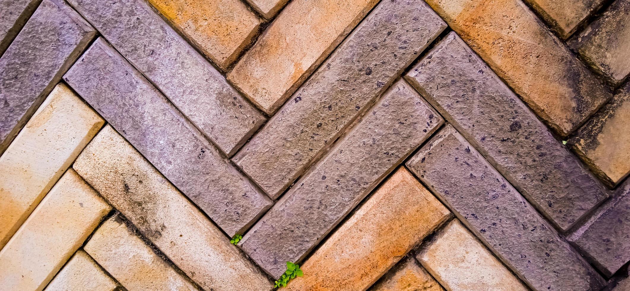 de gele en oranje achtergrond van het de tegelpatroon van de zigzagbaksteen met wat groen en bruin mos groeit op de baksteenoppervlakken. beschikbaar voor tekst. geschikt voor de bouw, architectuur, woondecoratie inspiratie foto