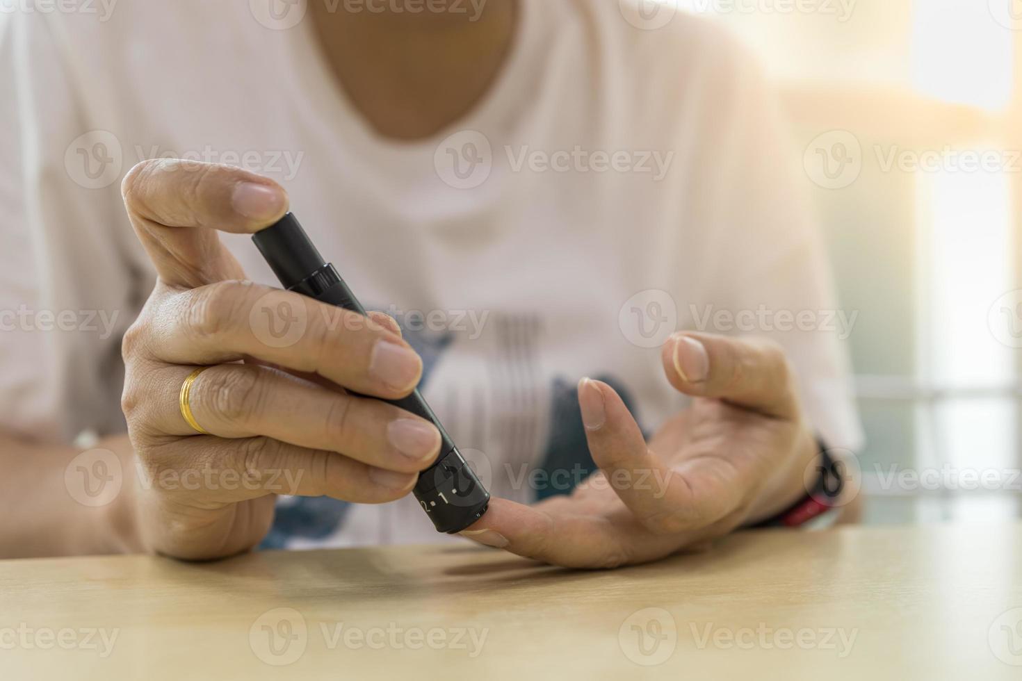 close-up van de handen van de mens met behulp van lancet op de vinger om de bloedsuikerspiegel te controleren met een glucosemeter. gebruik als medicijn, diabetes, glycemie, gezondheidszorg en mensenconcept. foto