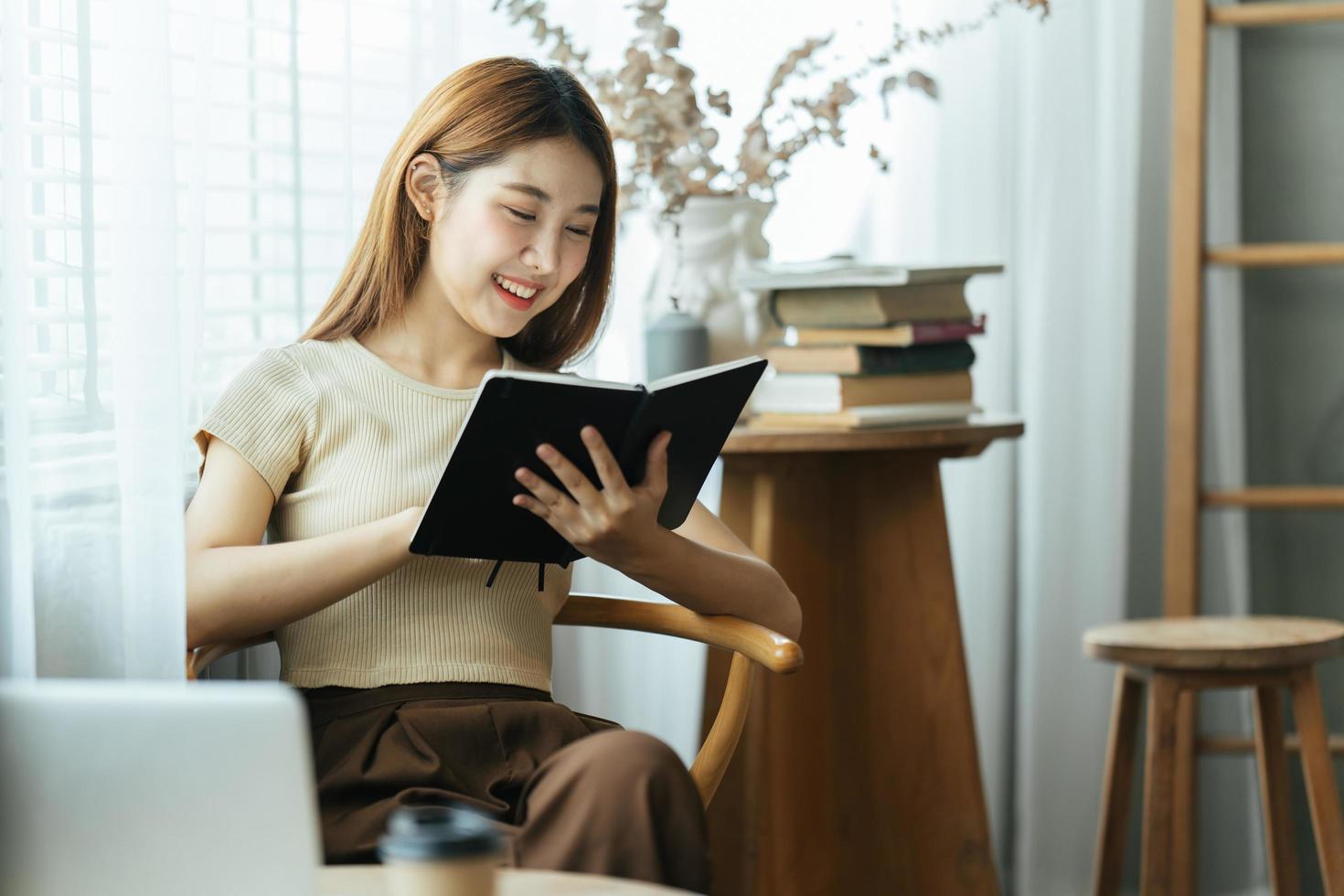 jonge Aziatische zakenvrouw zit aan een bureau en maakt aantekeningen in een notitieblok. het concept van onderwijs en technologie. foto