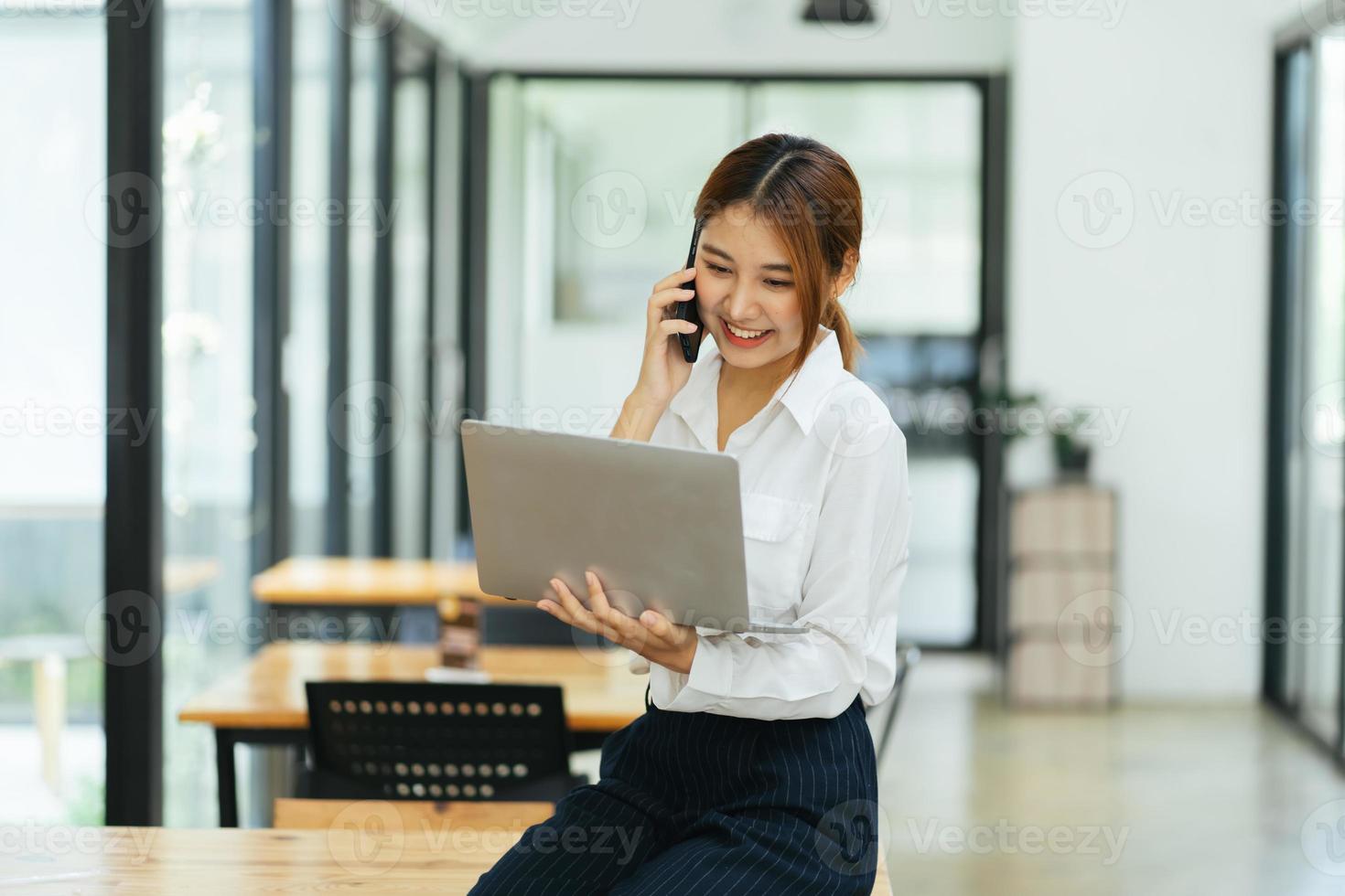 Aziatische zakenvrouw in formeel pak op kantoor blij en opgewekt tijdens het gebruik van smartphone en werken foto