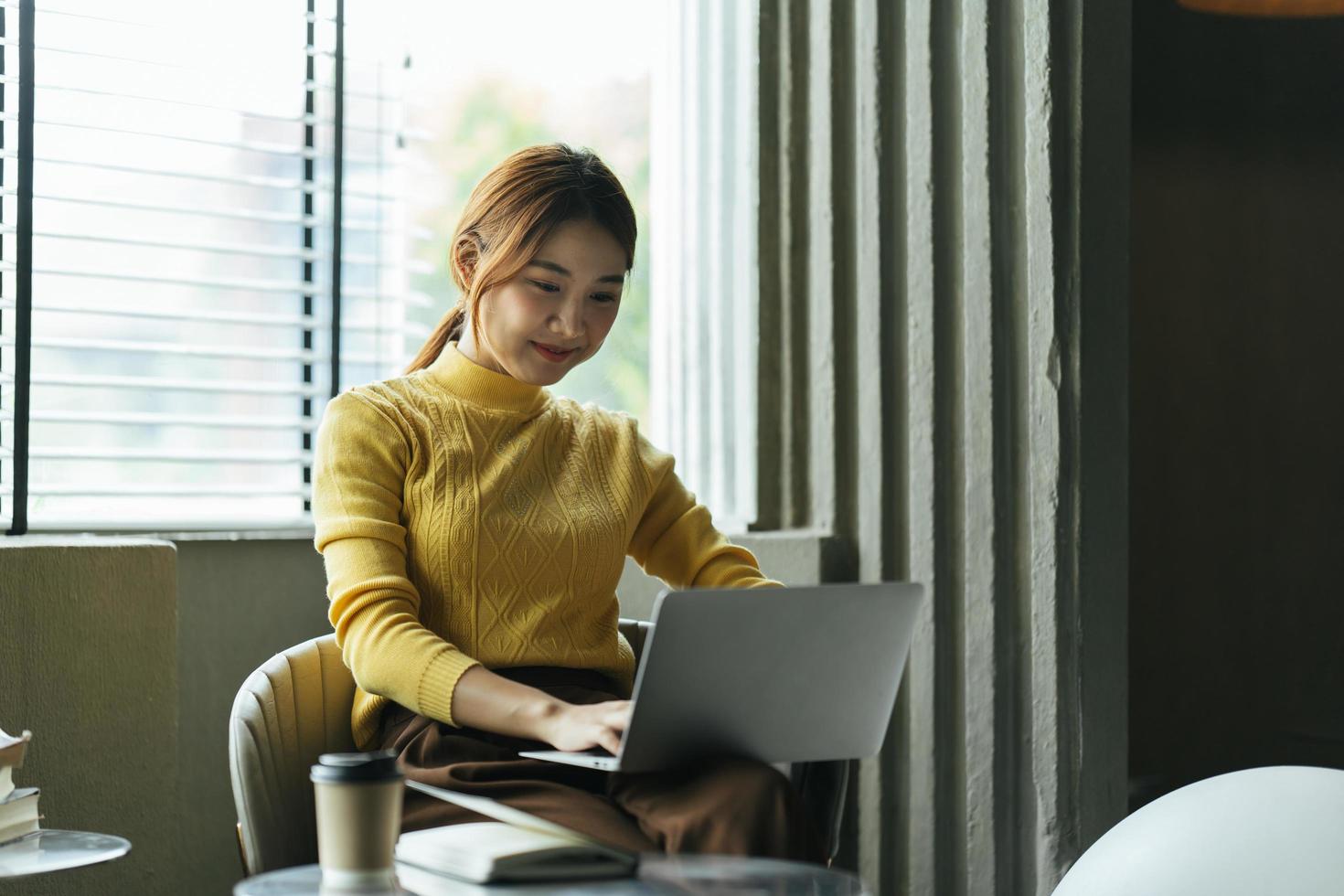 portret van een mooie aziatische vrouw die in de zomer binnenshuis in een coffeeshoprestaurant zit, met behulp van slimme draadloze technologie computerlaptop en smartphone, een ontspannende koffiepauze in het café-restaurant. foto